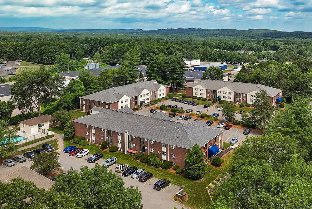 Aerial view of a vibrant apartment complex surrounded by lush greenery, showcasing ample parking and a serene community pool.