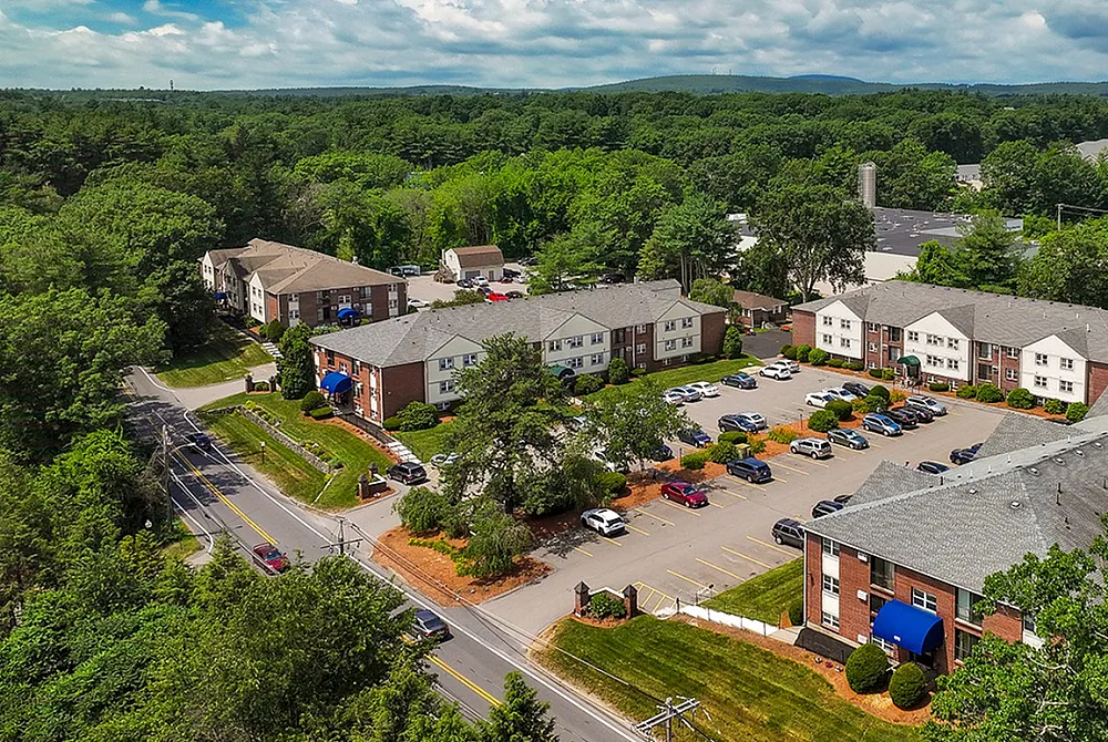 Charming apartment complex nestled within lush greenery, featuring modern buildings with ample parking, surrounded by scenic views.