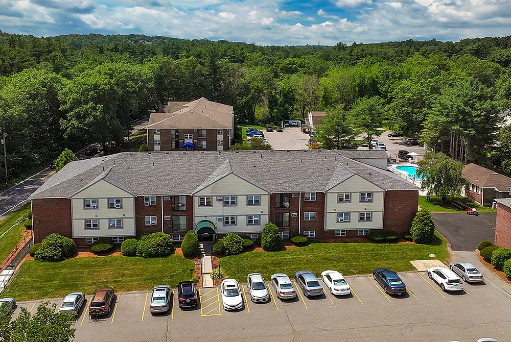 Charming apartment complex set against lush greenery, featuring well-manicured lawns, convenient parking, and a refreshing swimming pool.