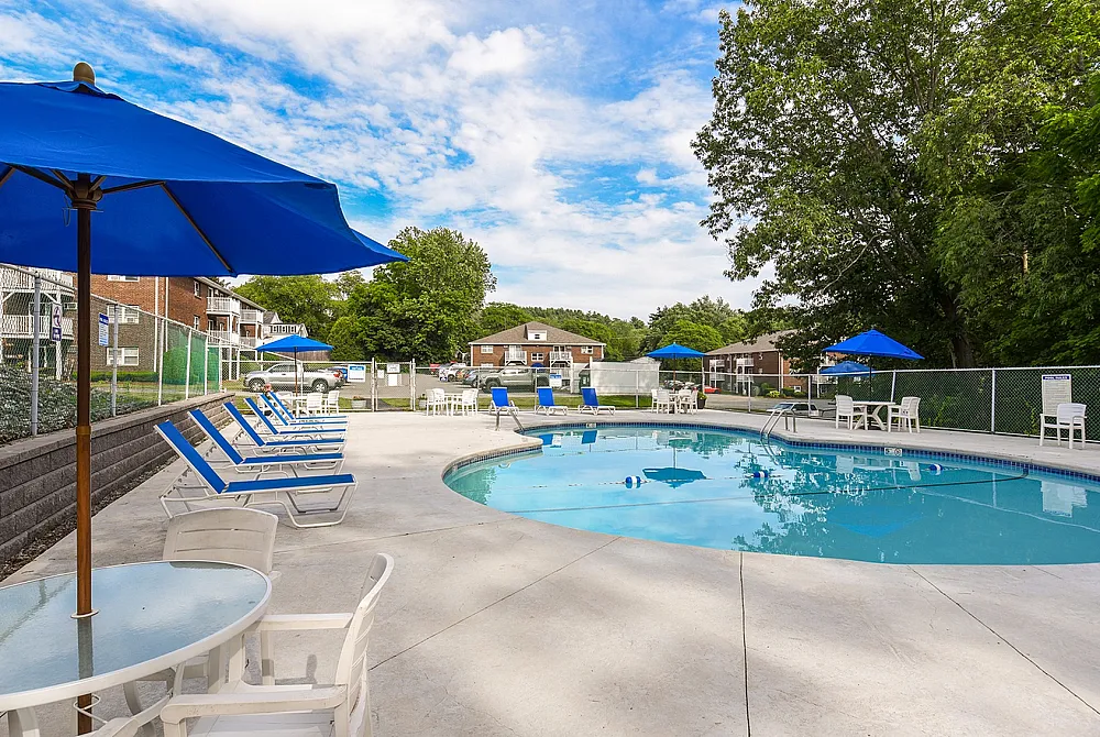 Inviting outdoor pool area with relaxing lounge chairs and vibrant blue umbrellas in a serene apartment community setting.