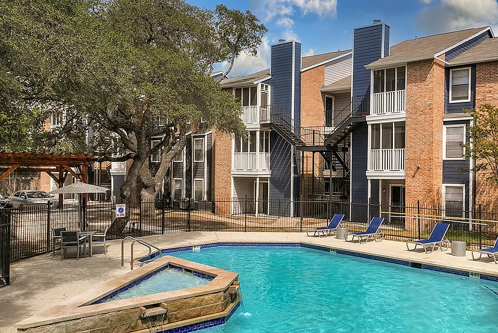 Charming apartment complex with inviting pool area, surrounded by lush greenery and modern patio seating for relaxation.
