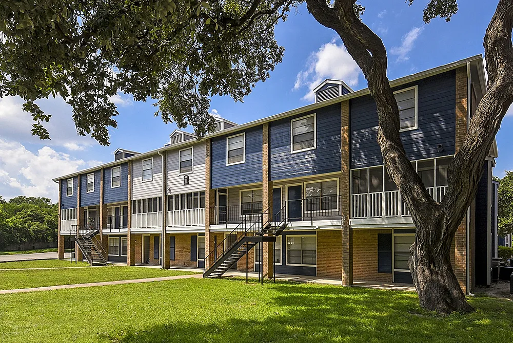 Charming apartment complex with stylish blue and white exterior, lush green surroundings, and inviting balconies, perfect for peaceful living.