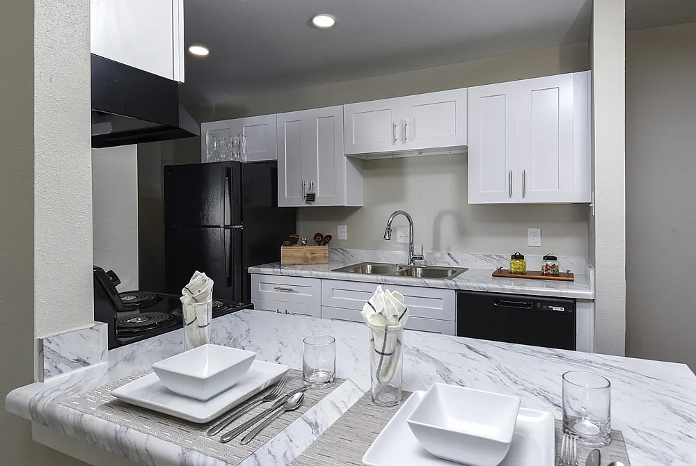 Modern kitchen with sleek white cabinetry, black appliances, and elegant marble countertops.