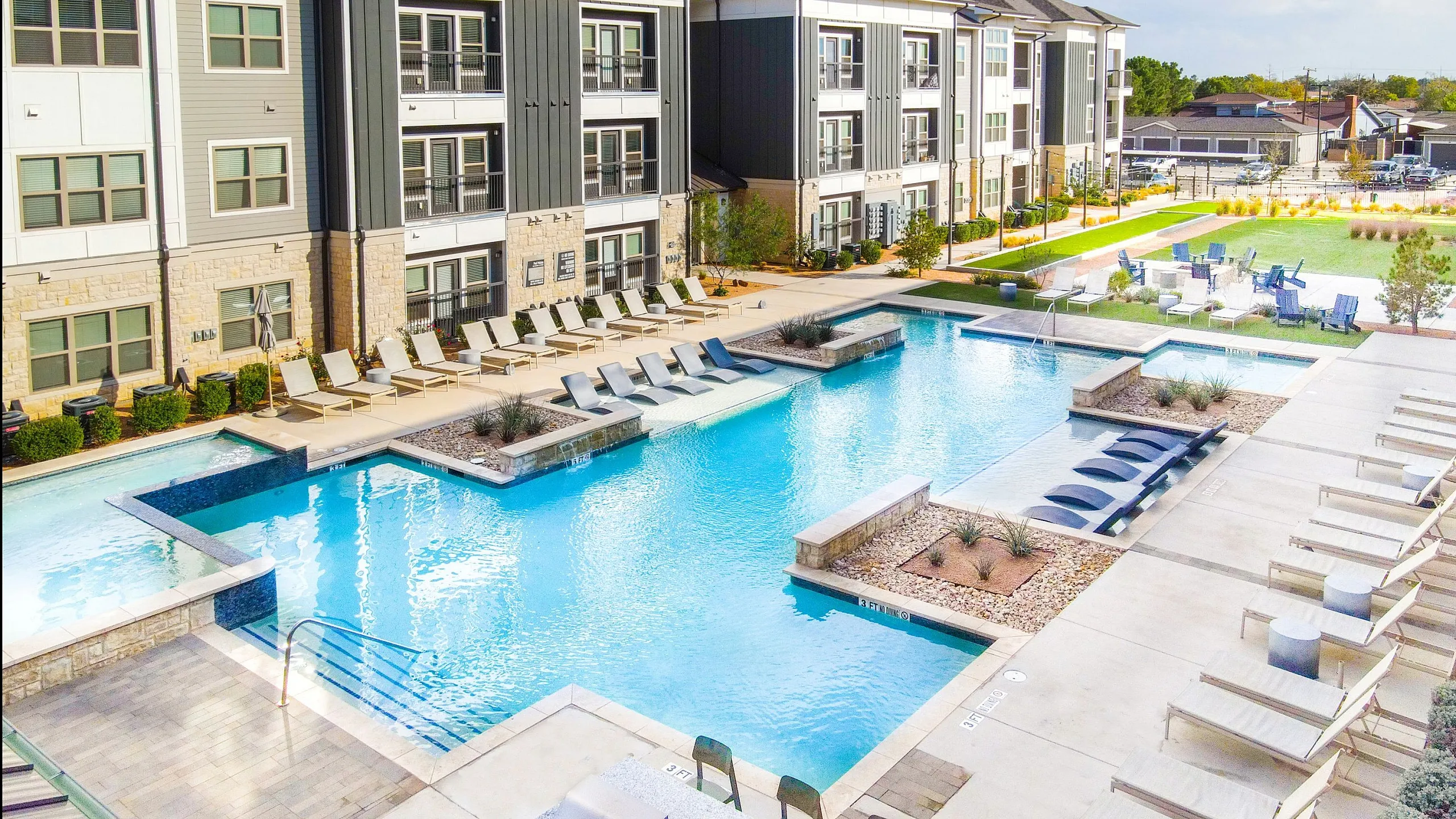 Luxurious apartment complex with a resort-style swimming pool, sun loungers, and lush greenery creating a serene outdoor oasis.