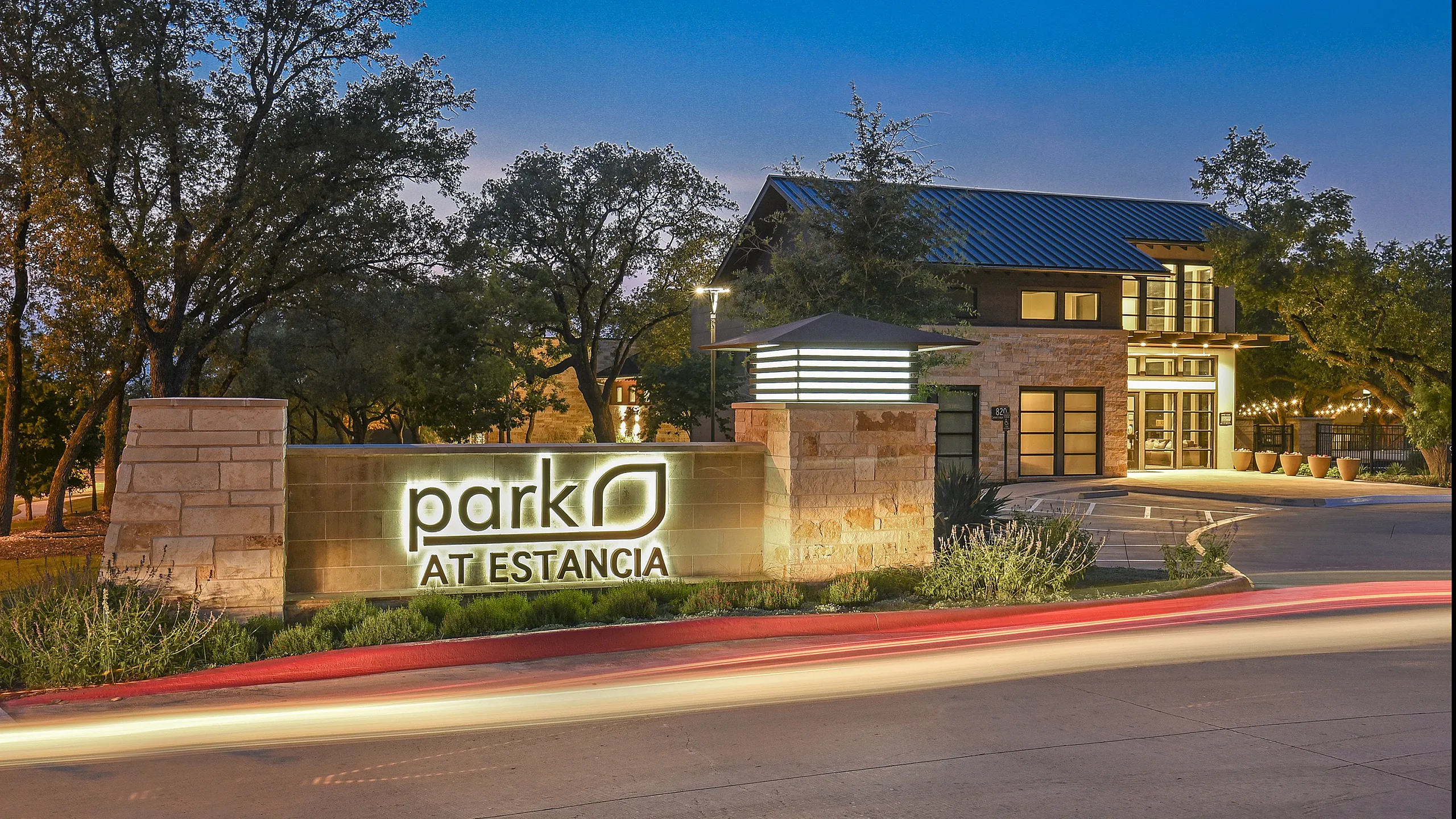 Elegant entrance of Park at Estancia, illuminated at dusk, featuring modern architecture amidst a lush, serene landscape.