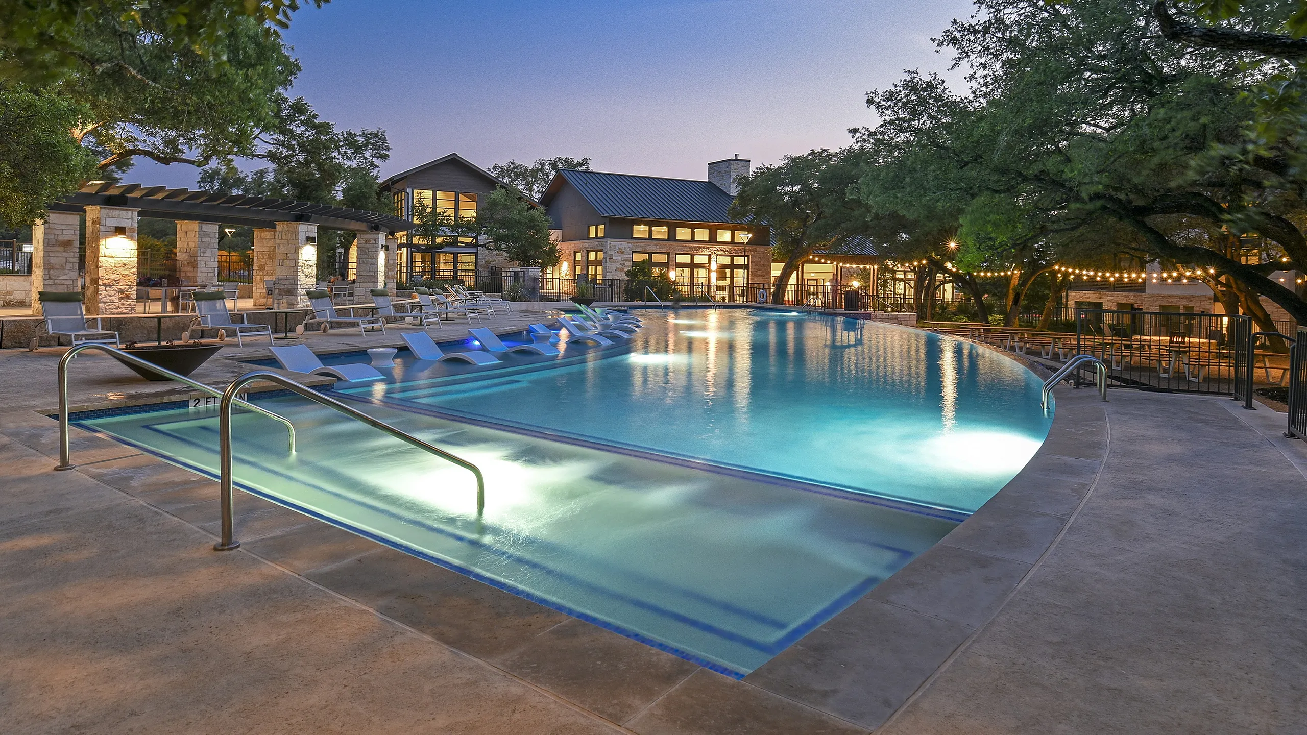 Stunning apartment complex with a luxurious outdoor pool, surrounded by lounge chairs and vibrant evening lights, perfect for relaxation and entertainment.