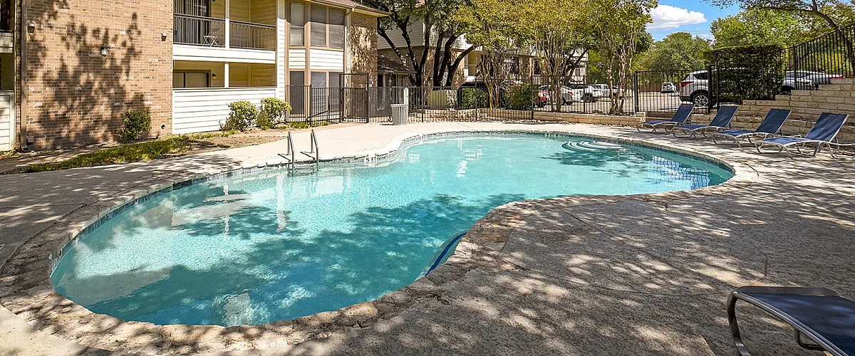 Charming apartment complex featuring a refreshing outdoor pool surrounded by lush greenery and comfortable lounge chairs.