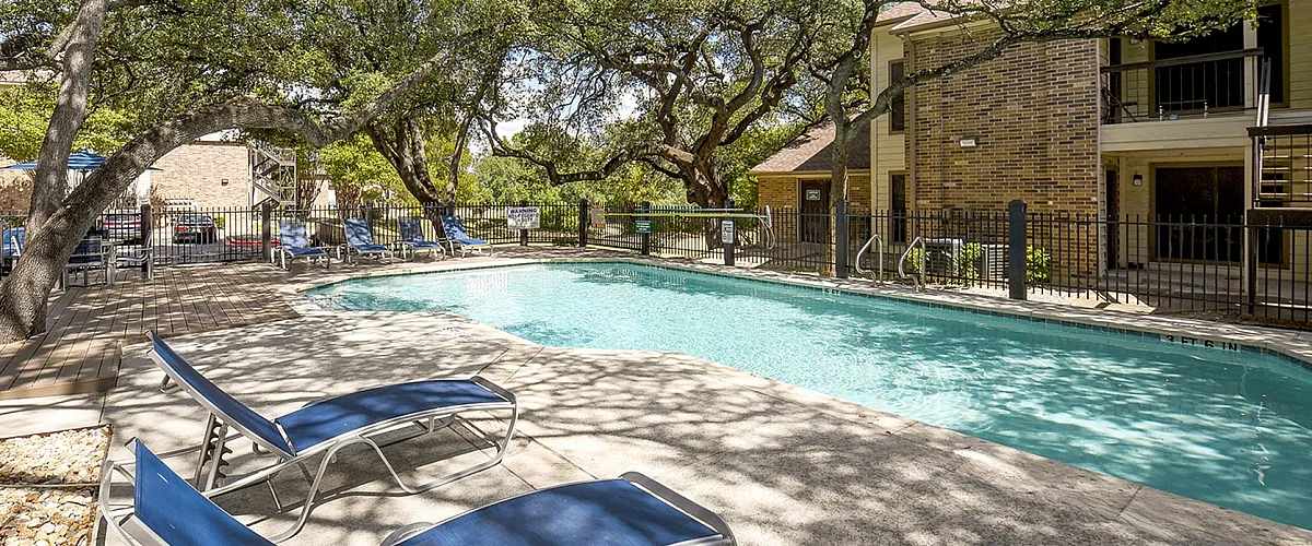 Inviting outdoor pool area surrounded by lush greenery and cozy lounge chairs, perfect for relaxation in a serene apartment complex.