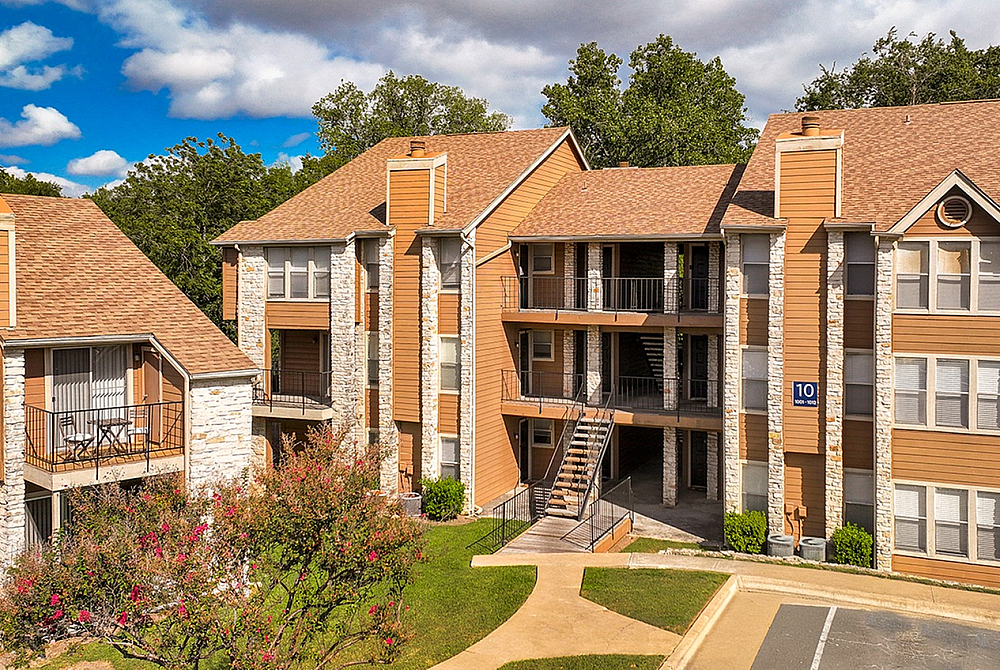 Charming apartment complex with stone and wood exterior, featuring multiple balconies and surrounded by lush greenery.