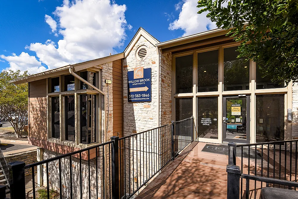 Inviting exterior of Willow Brook Apartments leasing office with rustic brick design and large windows under a bright blue sky.