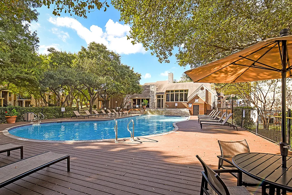 Inviting outdoor oasis featuring a sparkling swimming pool, surrounded by lush trees and stylish lounge chairs, with a shaded patio area perfect for relaxation.
