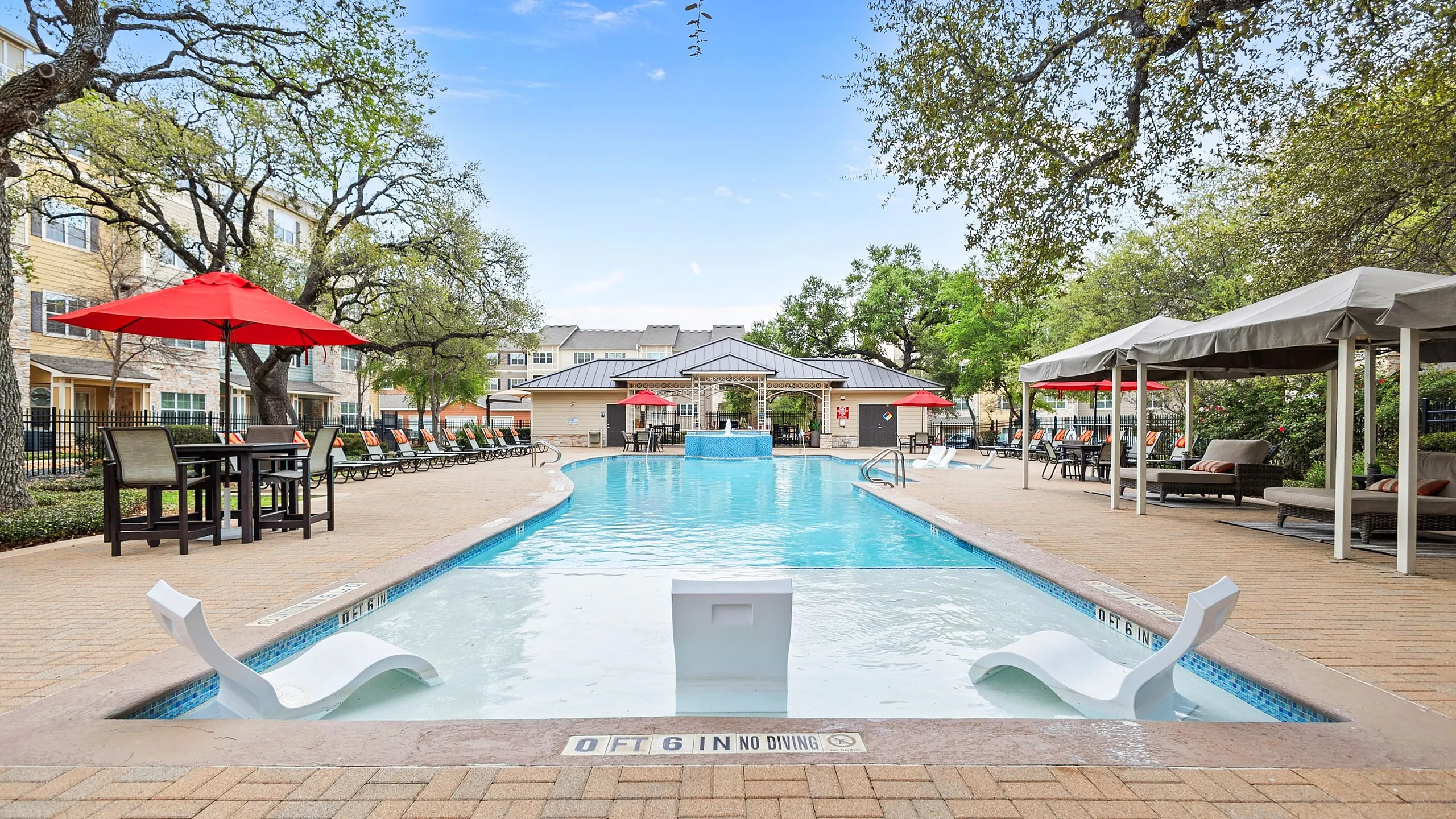Inviting outdoor pool area with relaxing lounge chairs, vibrant red umbrellas, and lush greenery, perfect for leisure and entertainment.