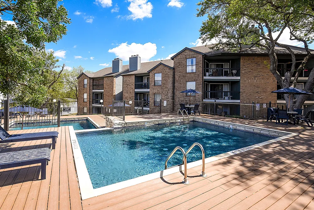 Inviting apartment complex with a luxurious swimming pool, sunlit deck, and elegant outdoor seating, perfect for relaxation.