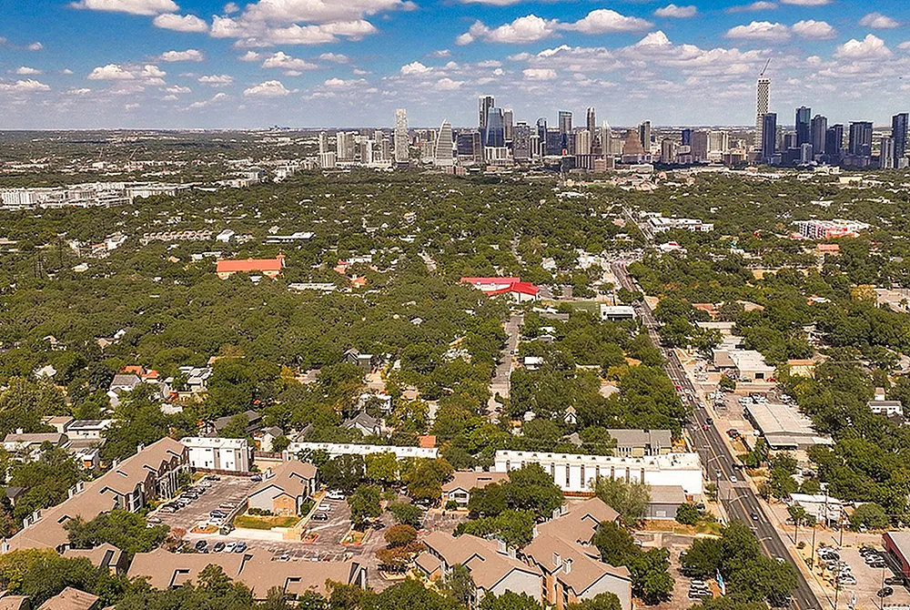 Vibrant aerial view showcasing a bustling cityscape surrounded by lush green suburbs and a clear blue sky.