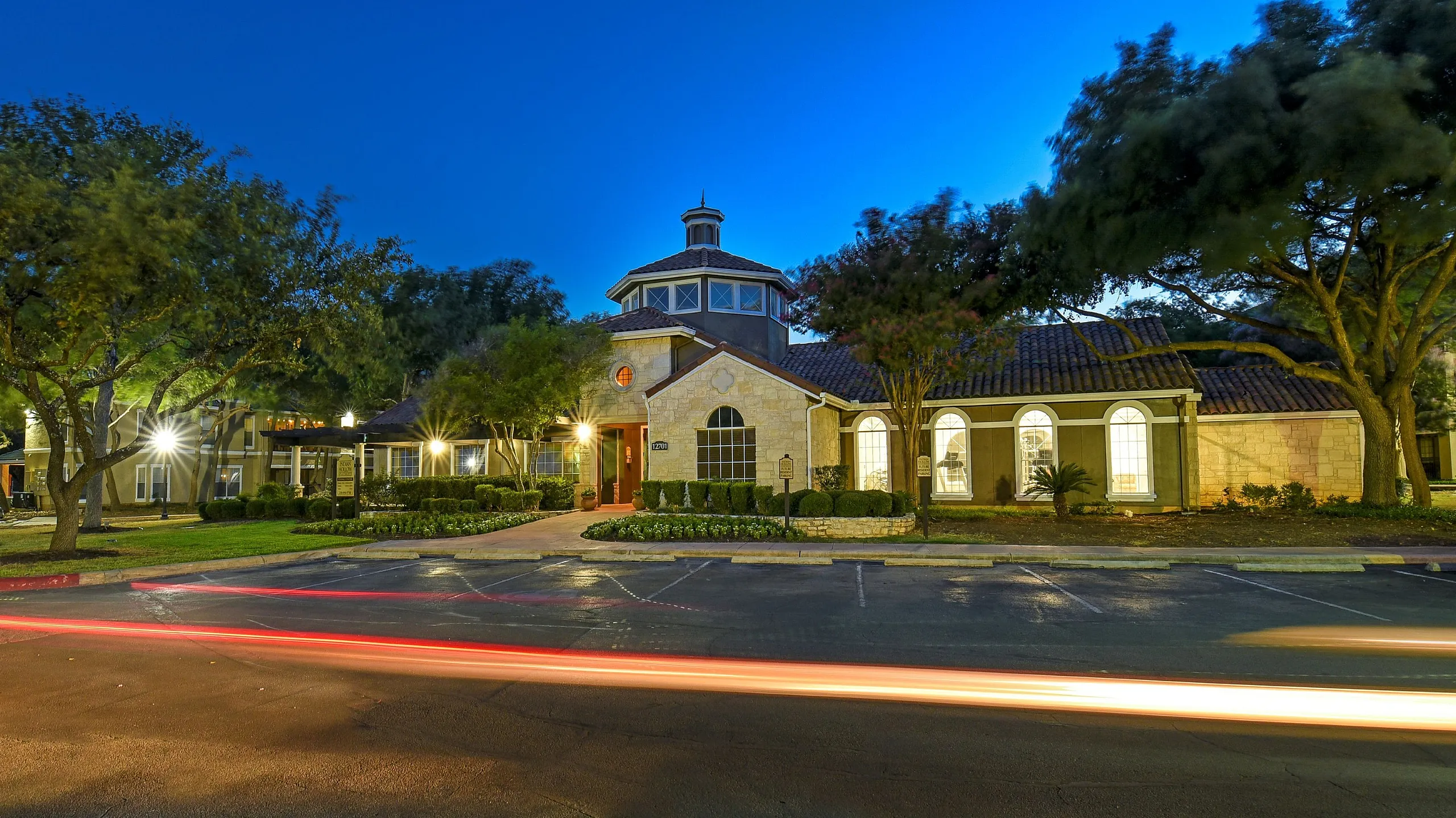 Inviting evening view of a charming apartment complex with elegant architecture and lush landscaping, highlighted by soft outdoor lighting.