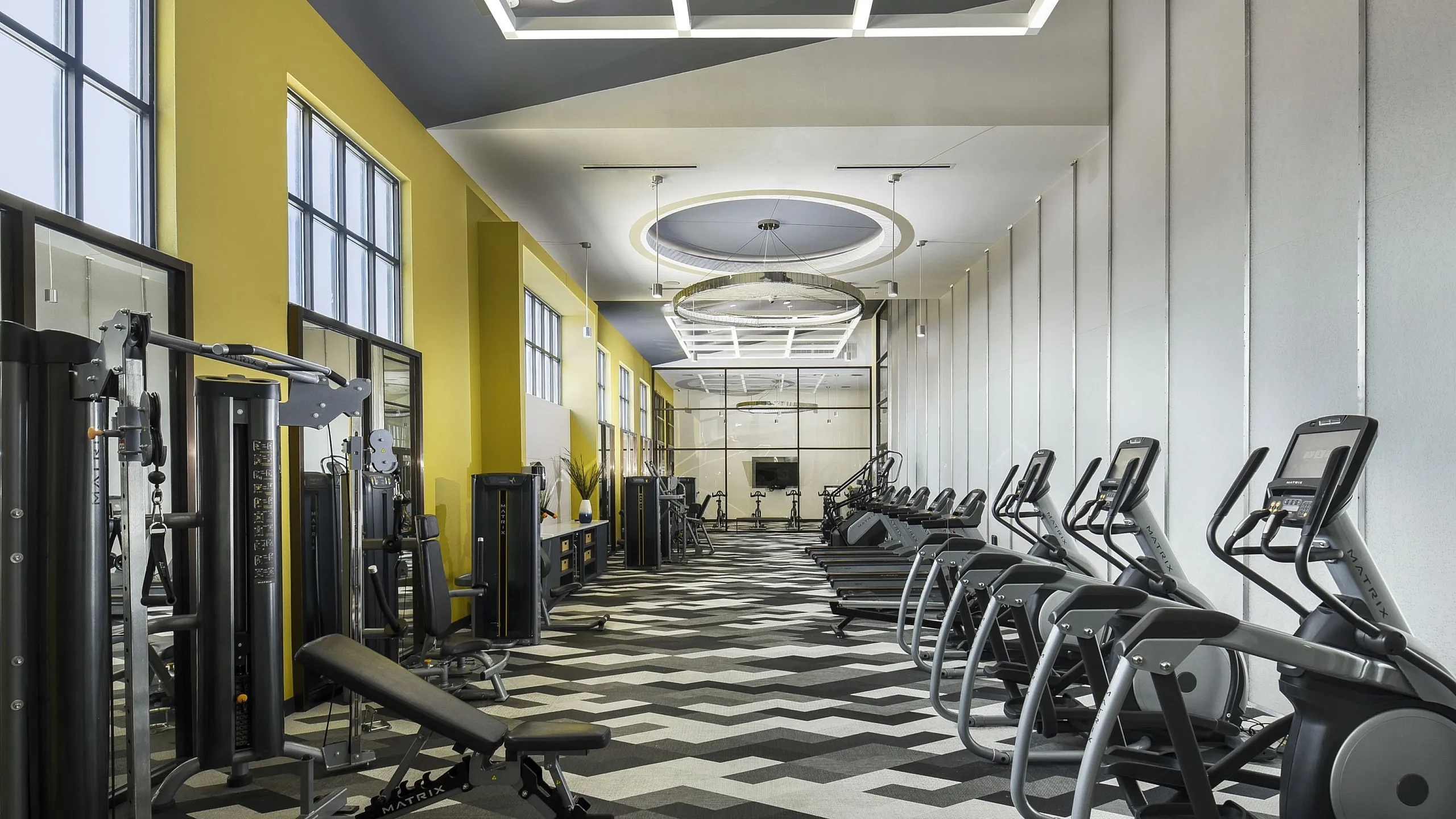 Modern apartment fitness center featuring state-of-the-art cardio machines and sleek strength training equipment, set in a stylish space with vibrant yellow accents.