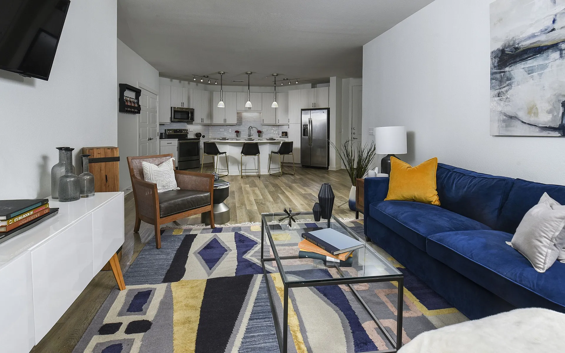 Modern open-concept living room with vibrant blue sofa, stylish geometric rug, and elegant kitchen featuring contemporary white cabinetry.