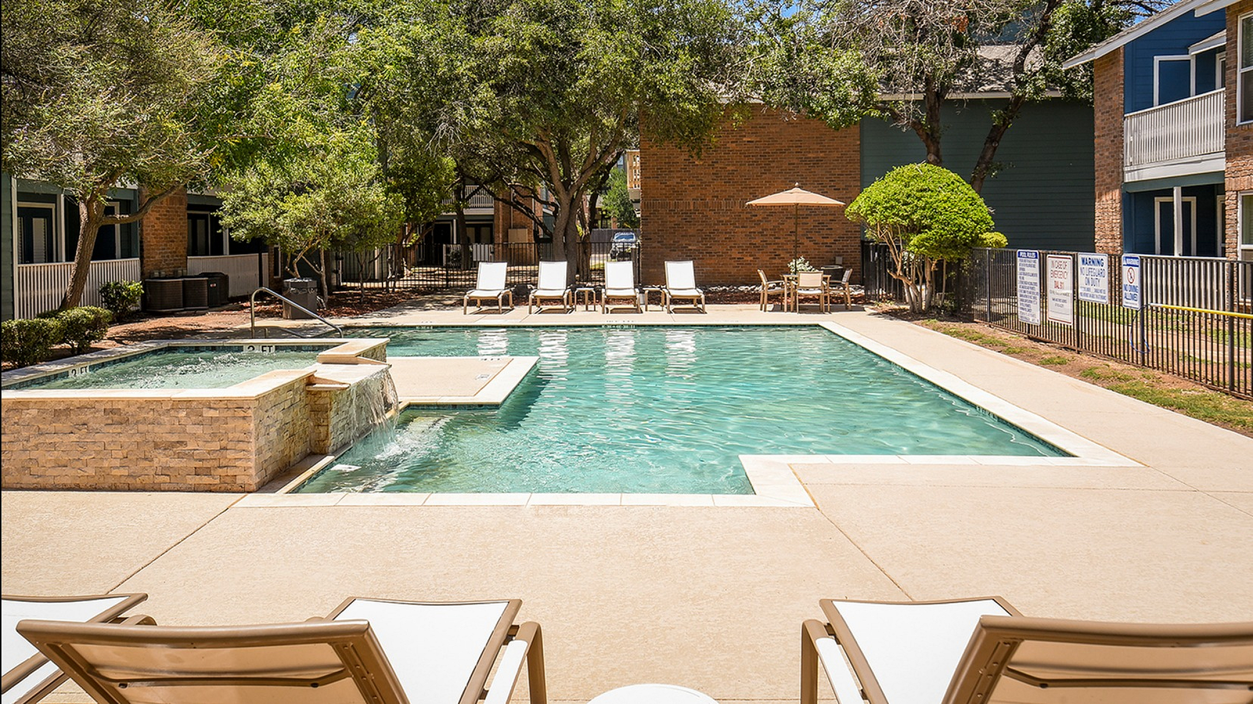 Inviting modern apartment pool area with sun loungers, surrounded by lush greenery and stylish architecture.
