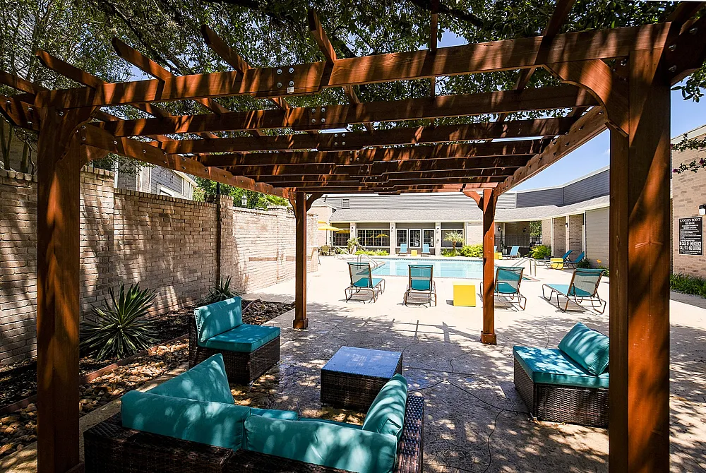 Inviting outdoor pool area with elegant wooden pergola, cozy turquoise seating, and sun-drenched loungers ideal for relaxation and leisure.
