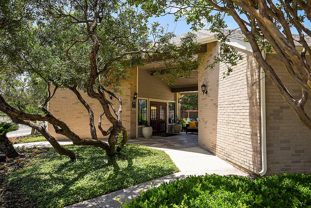Charming apartment entrance shaded by lush greenery and inviting outdoor seating.