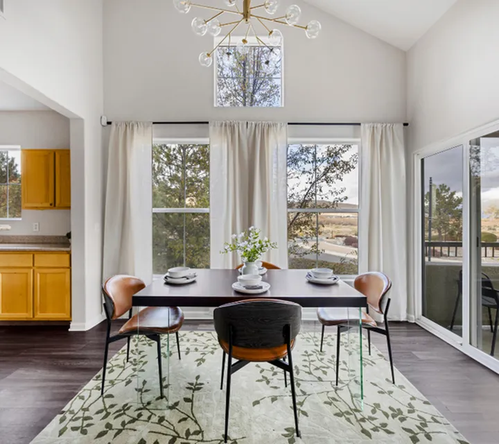 Modern dining room with stylish table set, large windows, and elegant chandelier