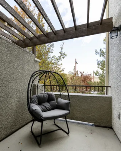 Charming balcony with cushioned hanging chair and pergola, offering a tranquil outdoor retreat.