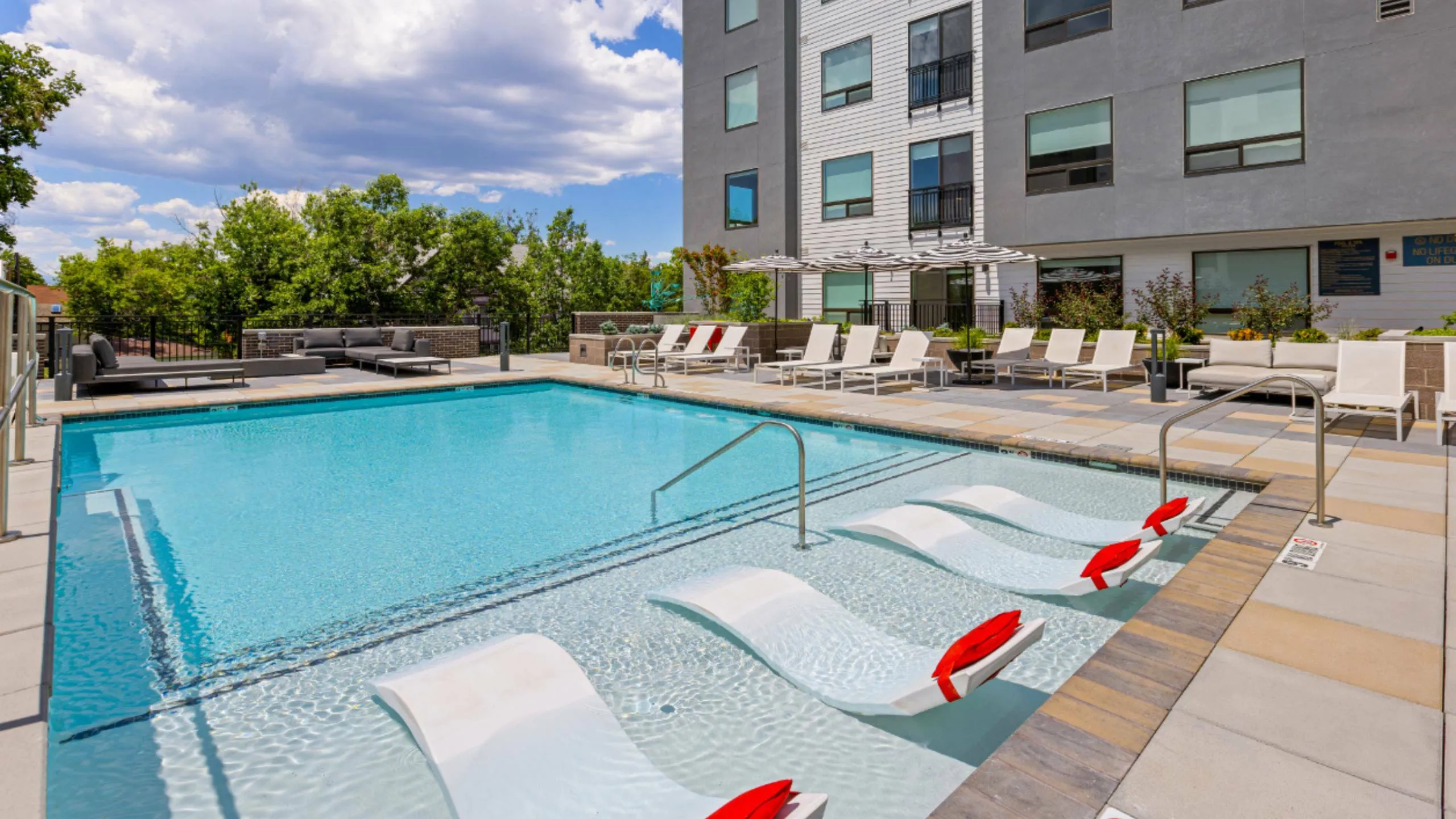 Modern apartment complex with luxurious outdoor pool area featuring sun loungers and greenery