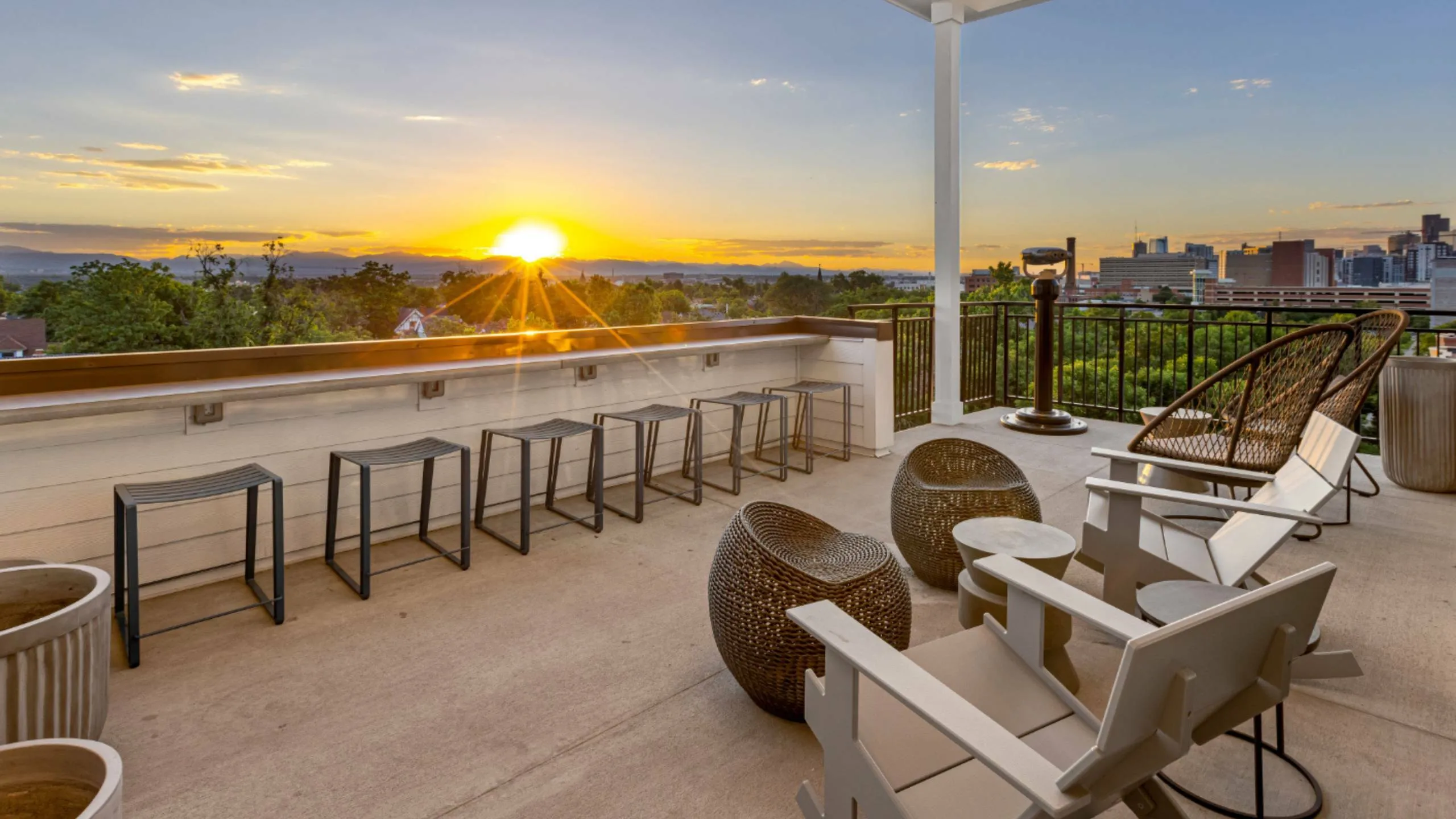 Stunning sunset view from a modern apartment terrace with stylish seating and cityscape in the background.