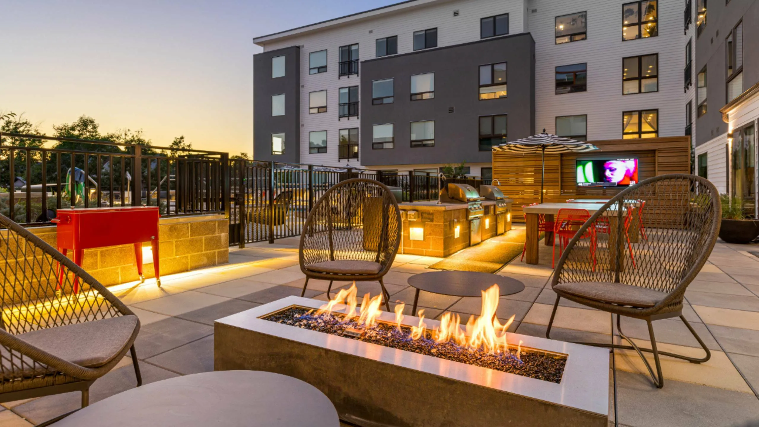Stylish outdoor lounge with cozy fire pit, modern seating, and sleek apartment backdrop at sunset.