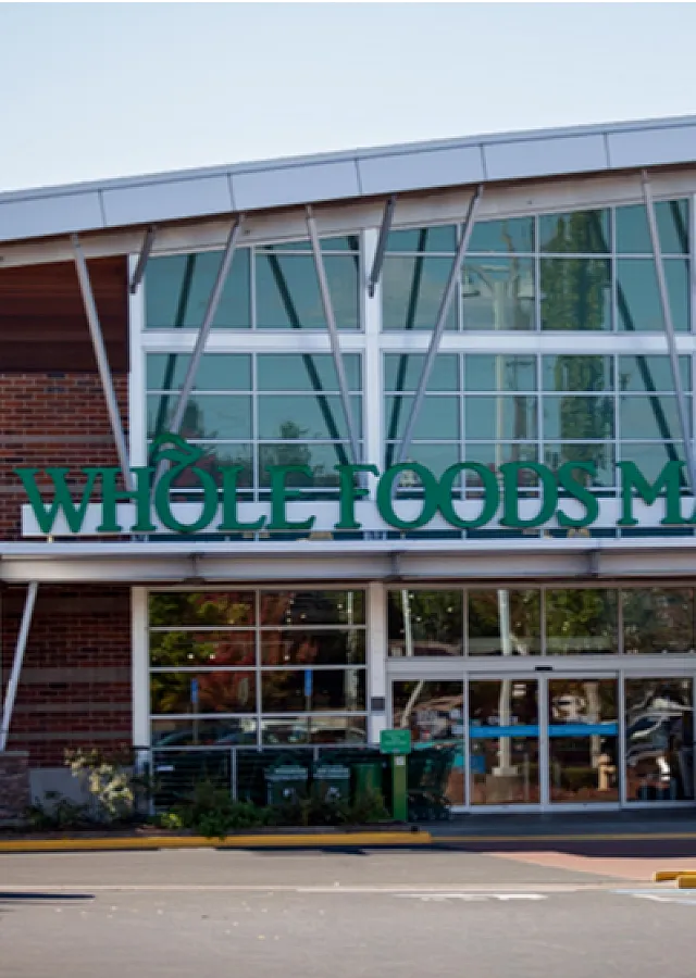 Front exterior of a modern Whole Foods Market with glass architecture and welcoming entrance.