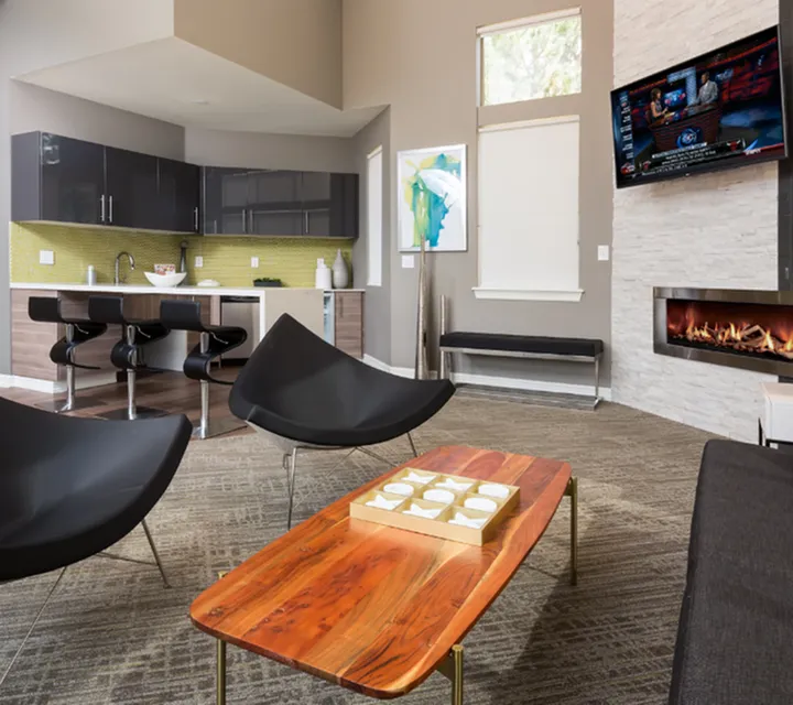 Contemporary open-concept living room with sleek black furniture, vibrant artwork, modern fireplace, and stylish kitchen area.