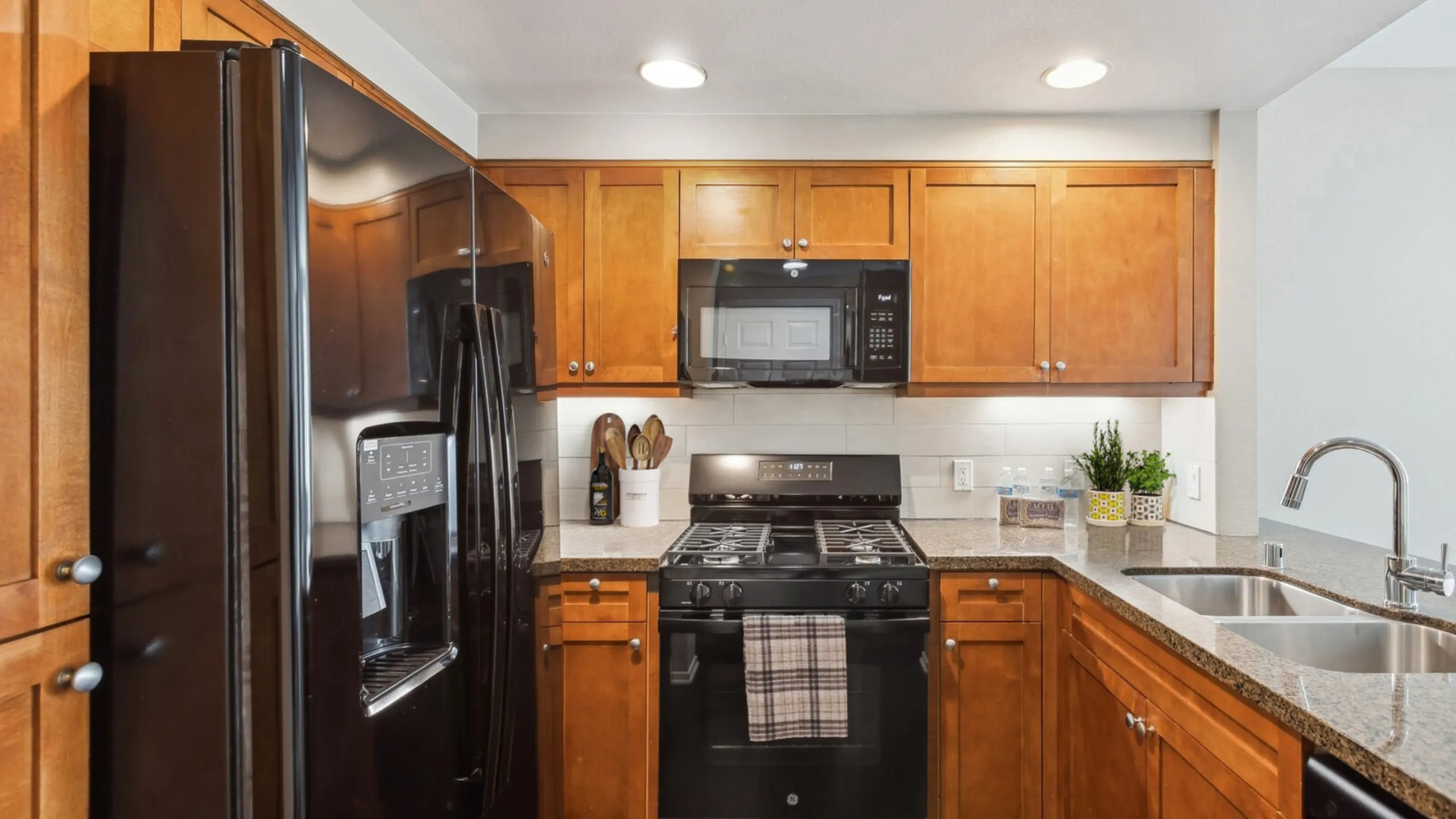 Modern kitchen with sleek black appliances, warm wood cabinetry, and granite countertops, offering a stylish and functional space for culinary creativity.