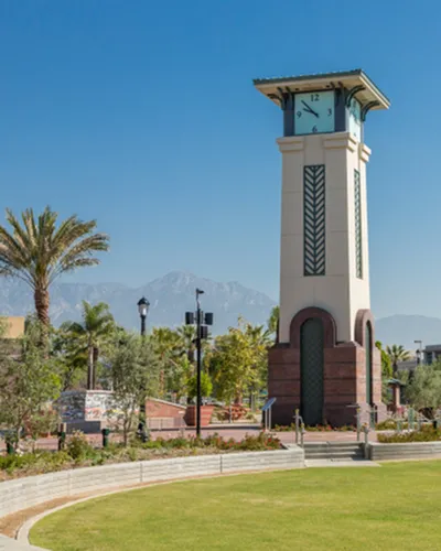 Charming clock tower amidst lush greenery with stunning mountain backdrop, offering a picturesque community setting.