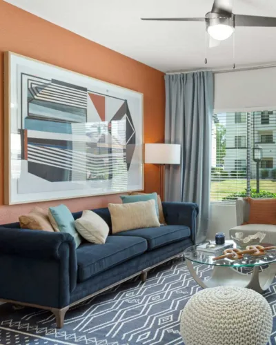 Chic living room featuring a navy plush sofa, geometric patterned rug, and modern artwork, bathed in natural light from large windows.