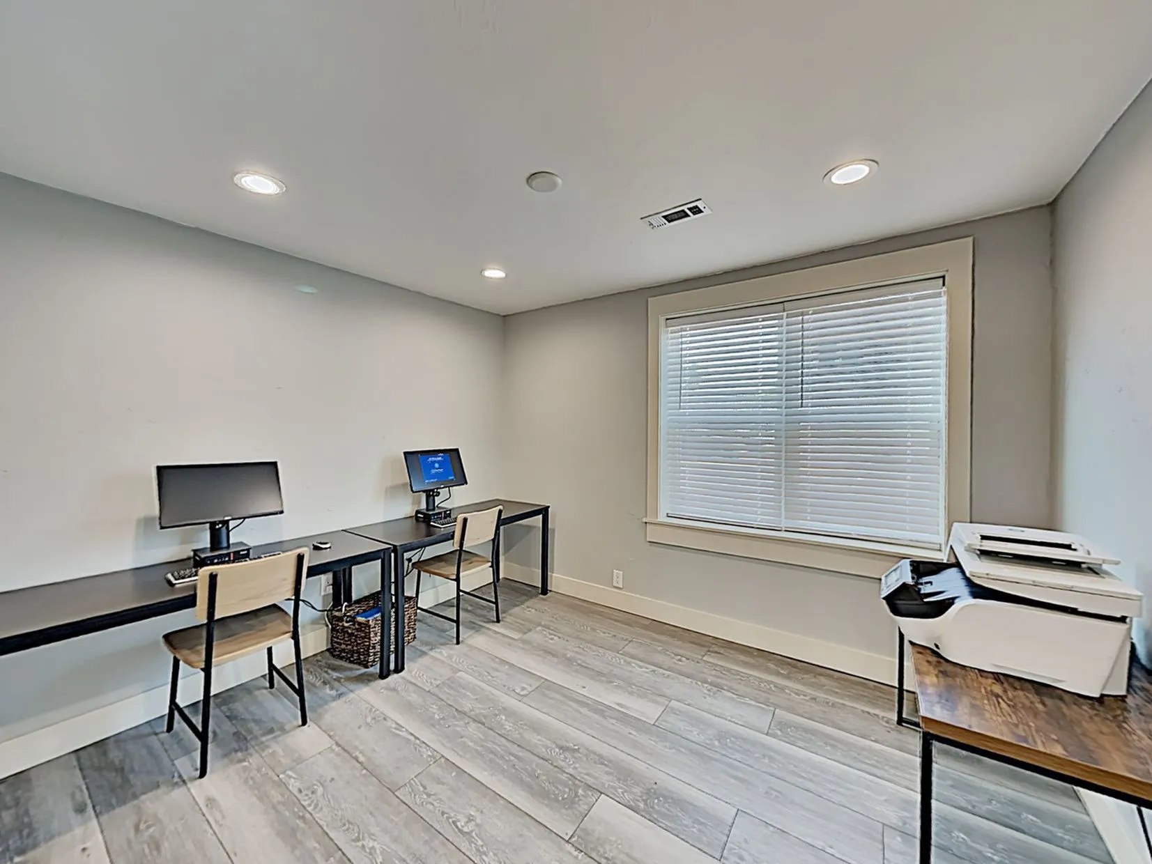 Modern home office space with sleek workstations, dual monitors, and natural light from a large window.