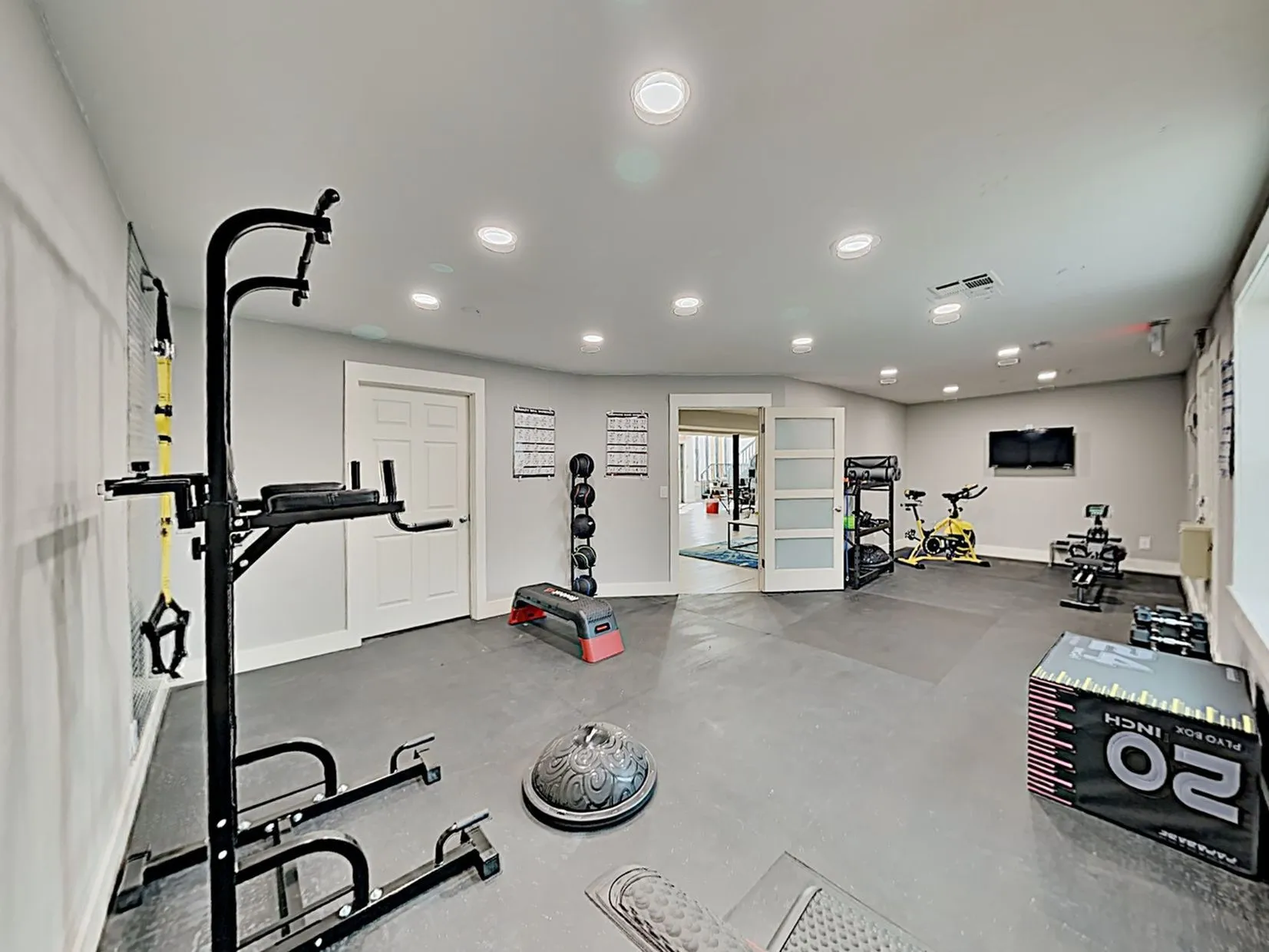 Spacious home gym featuring modern fitness equipment, including a weight rack, exercise bike, and ample workout space.
