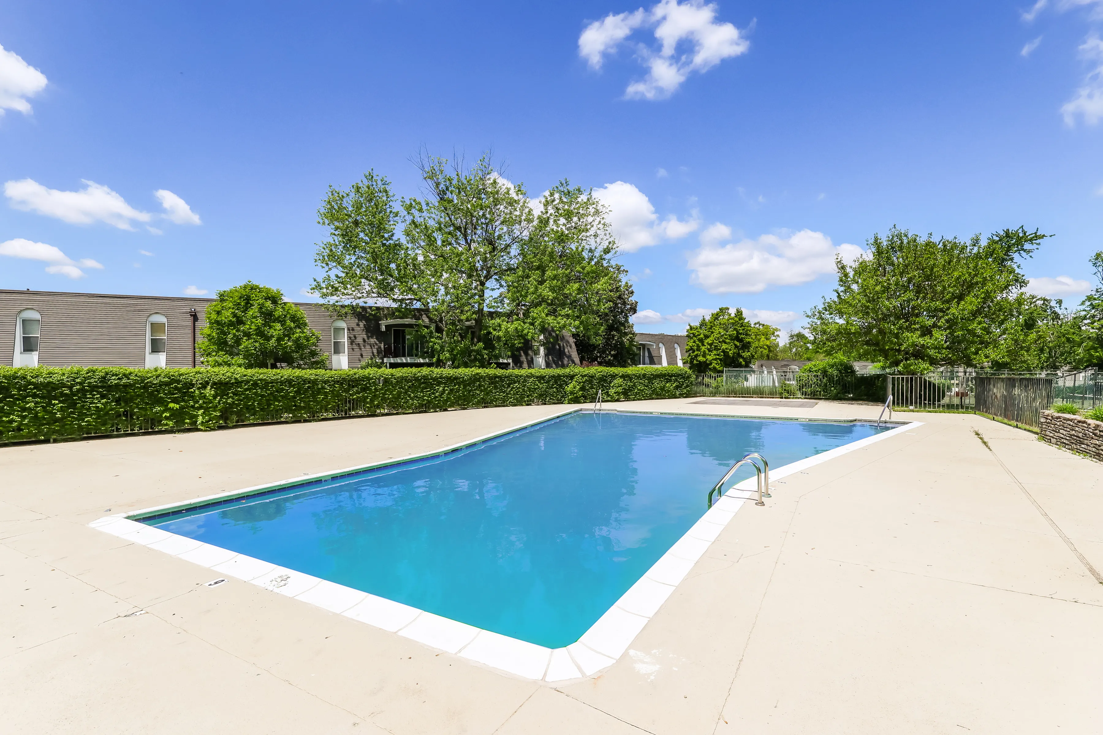 Inviting outdoor pool area with crystal clear water, surrounded by lush greenery and a sunny blue sky, perfect for relaxation and leisure.