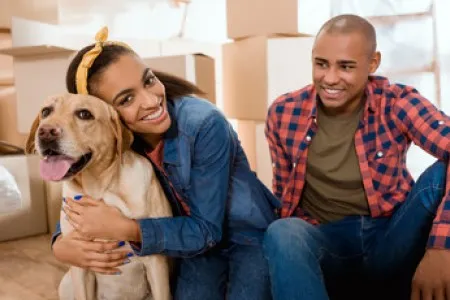 Happy couple with their dog surrounded by moving boxes, ready to start a new chapter in their modern, pet-friendly apartment.