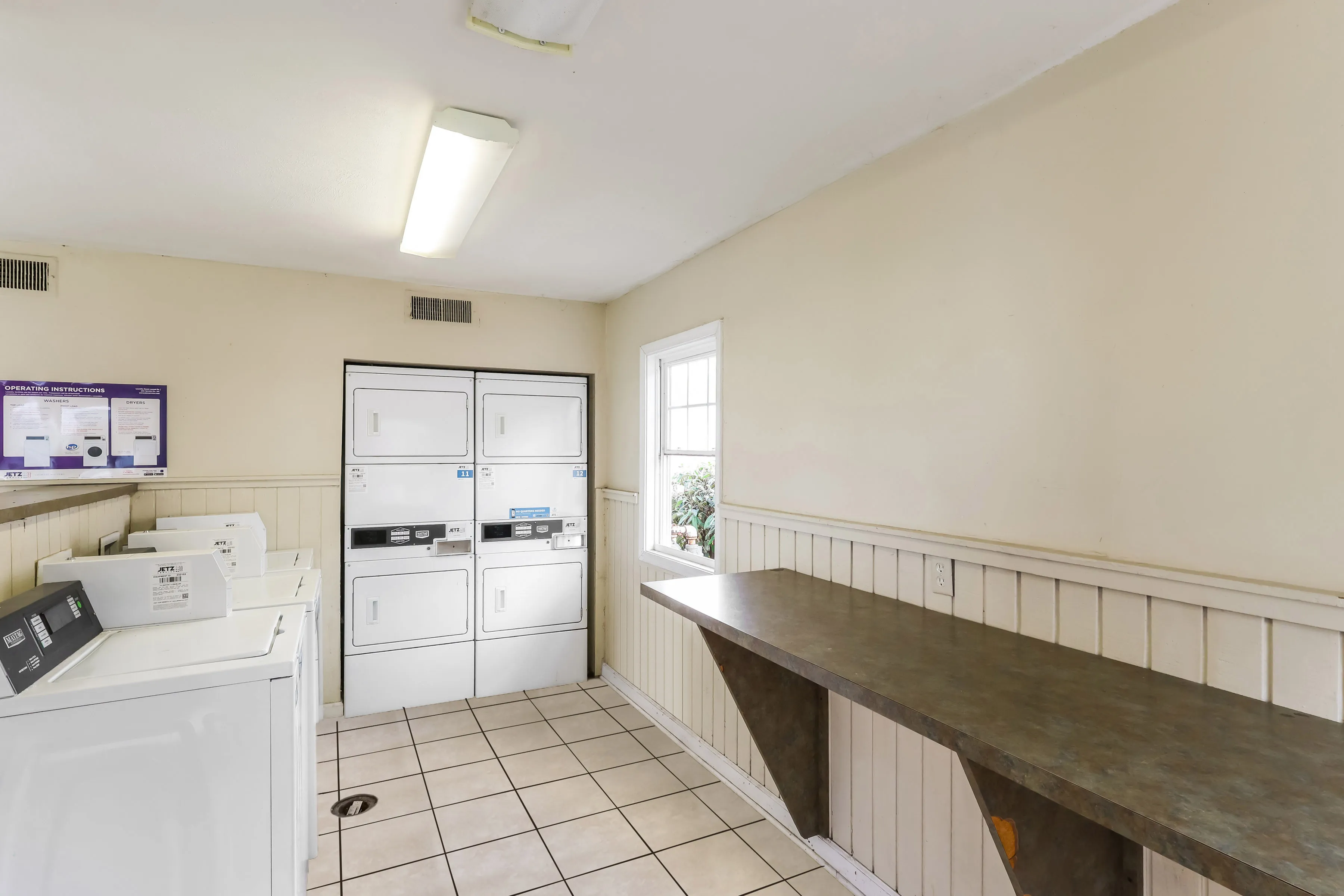Bright and functional laundry room with modern stacked washers and dryers, featuring a convenient folding counter and natural light from a window.