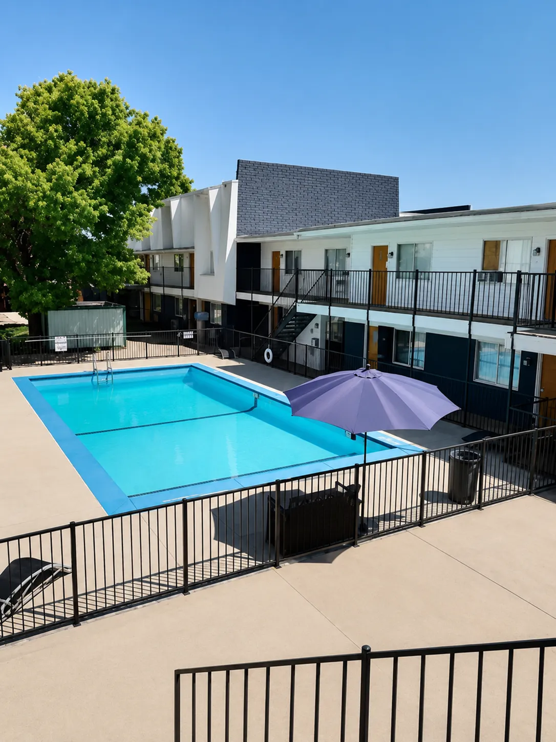 Chic apartment complex featuring a sunny pool area with modern fenced patio and a vibrant umbrella, perfect for relaxation.