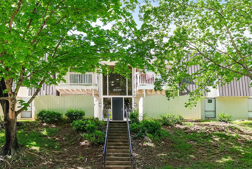 Inviting apartment exterior with lush greenery, charming balconies, and a welcoming entrance framed by vibrant trees.