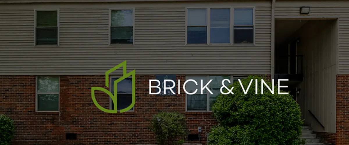 Charming apartment exterior featuring classic brick and siding, lush greenery, and the Brick & Vine logo, showcasing a welcoming community.