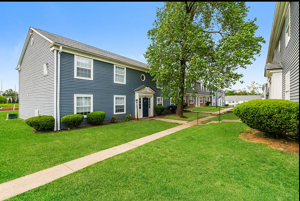 Charming apartment complex with blue siding, set in lush green surroundings, ideal for tranquil living.