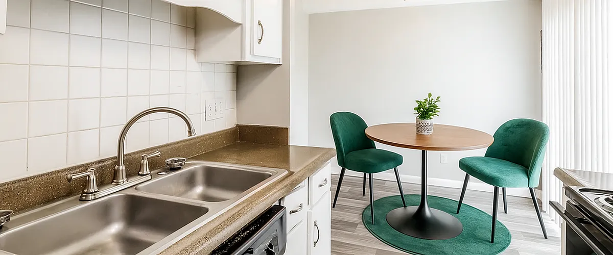 Inviting kitchen area with sleek countertops, modern sink, and cozy dining nook featuring green chairs and a round table.