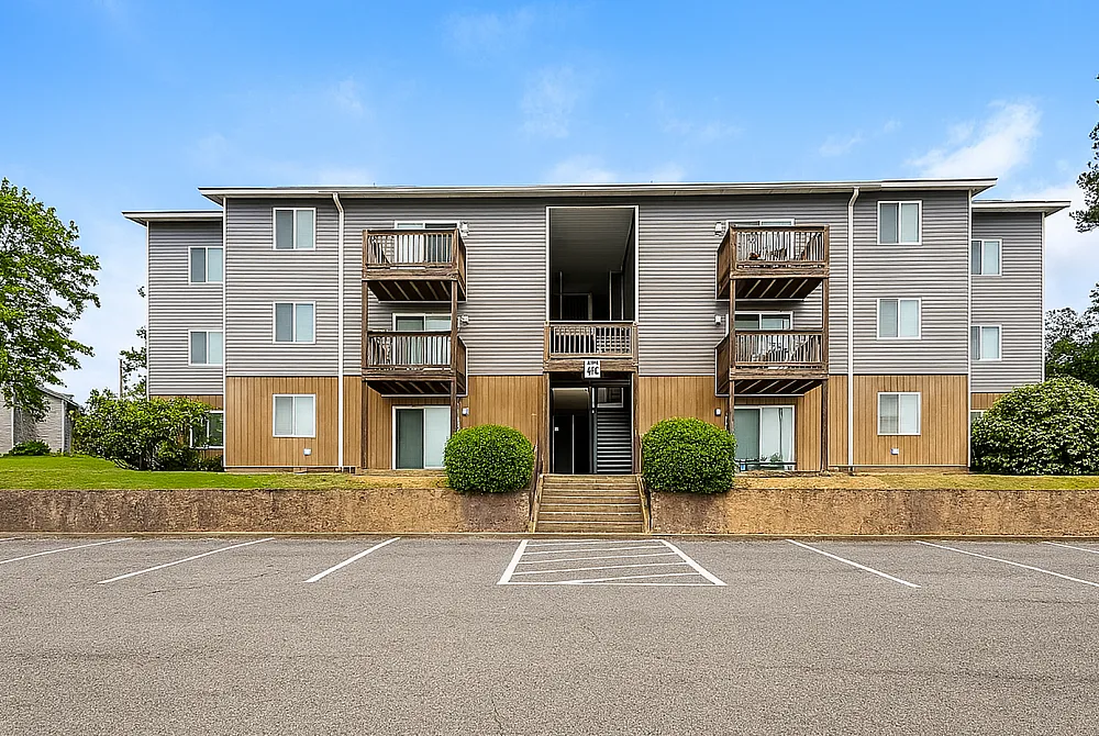 Charming apartment building with modern design and inviting balconies, surrounded by lush greenery, offering ample parking space.