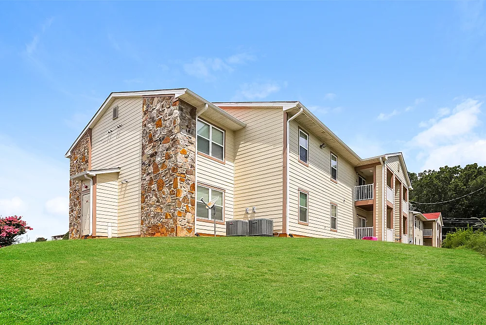 Charming two-story apartment building with stone accents and lush green lawn under a clear blue sky.
