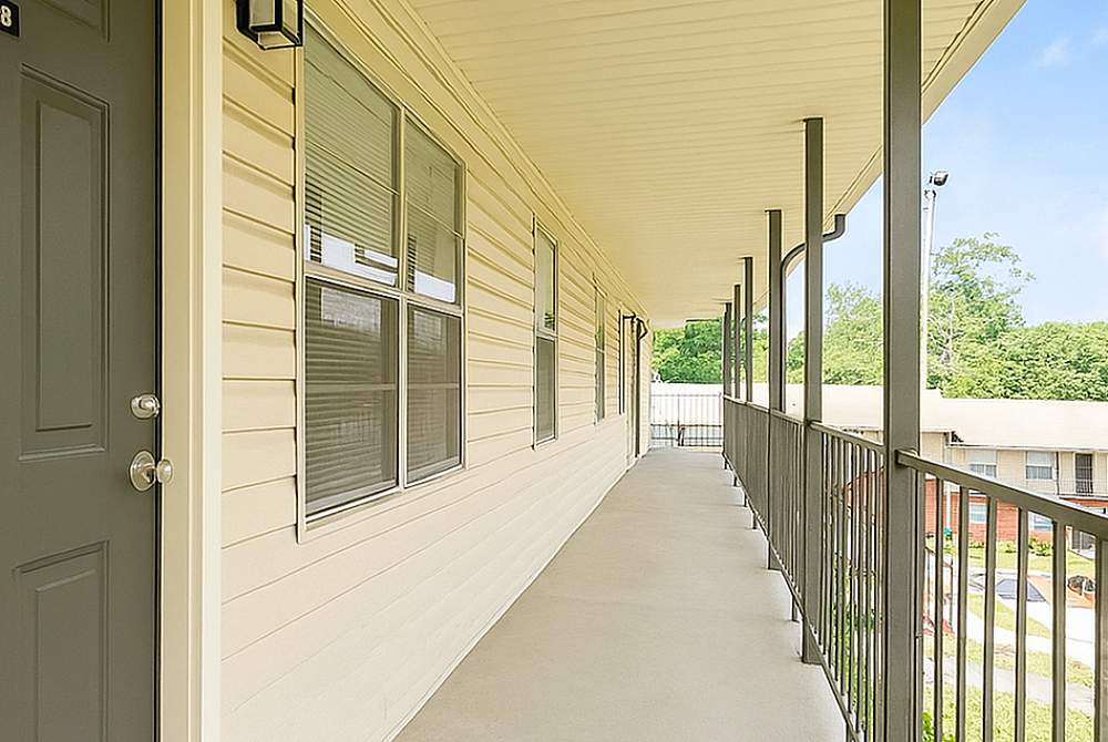 Inviting apartment walkway with modern railing and clean design, overlooking lush greenery and vibrant residential community.
