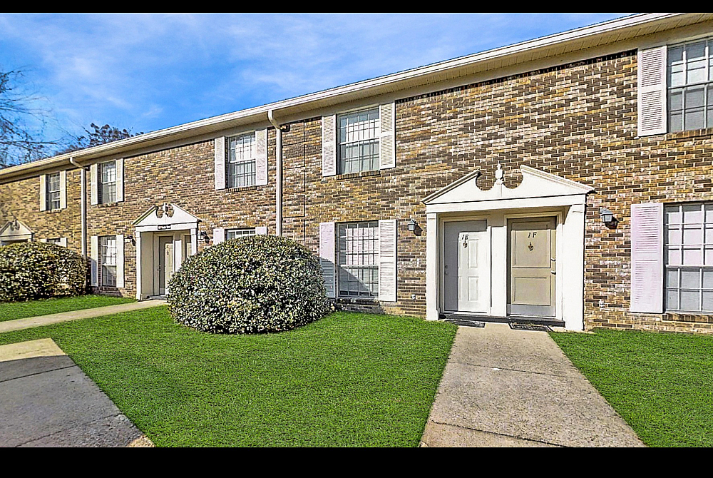 Charming brick townhouse featuring a classic facade with elegant white shutters, nestled in a lush, green setting.