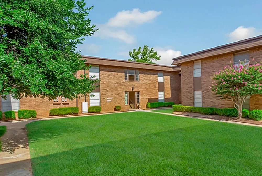 Charming apartment complex with lush green courtyard, surrounded by well-maintained brick buildings and vibrant landscaping.