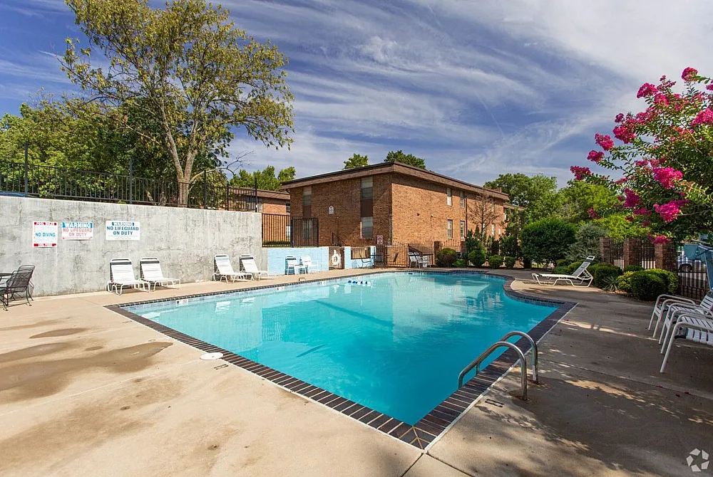 Inviting apartment complex with a sparkling outdoor pool, surrounded by lush greenery and sun loungers, perfect for relaxation.